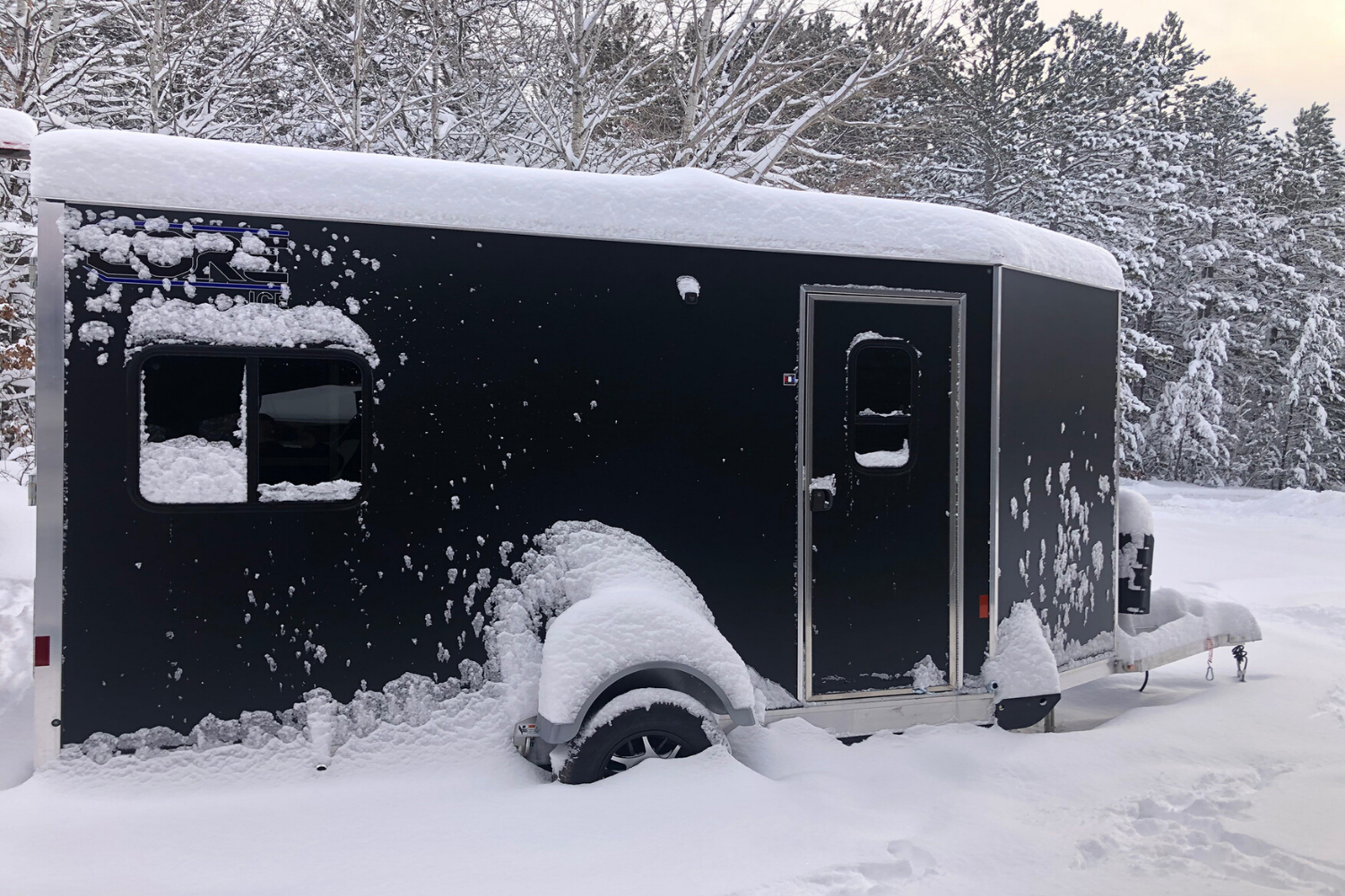 Red CORE ICE trailer set outside on the ice at night behind a four wheeler with tracks on it, a cooler set out front and the LED lights on