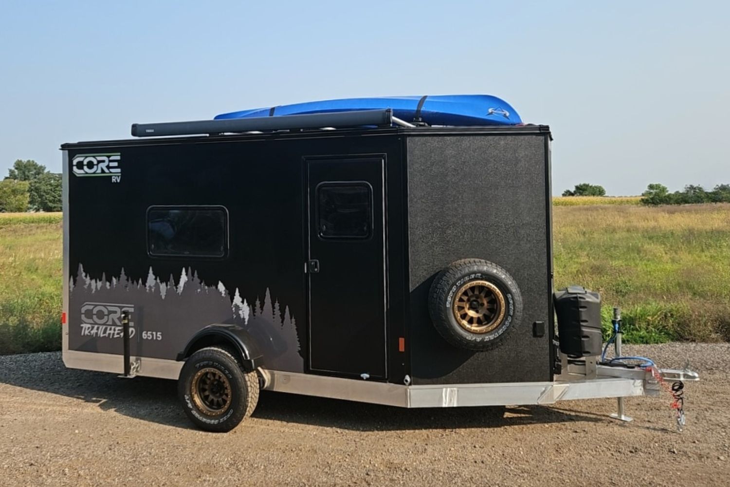 Exterior view of the CORE RV 6515 Trailhead curbside with grey tree graphics and awning on the roof and a mounted kayak
