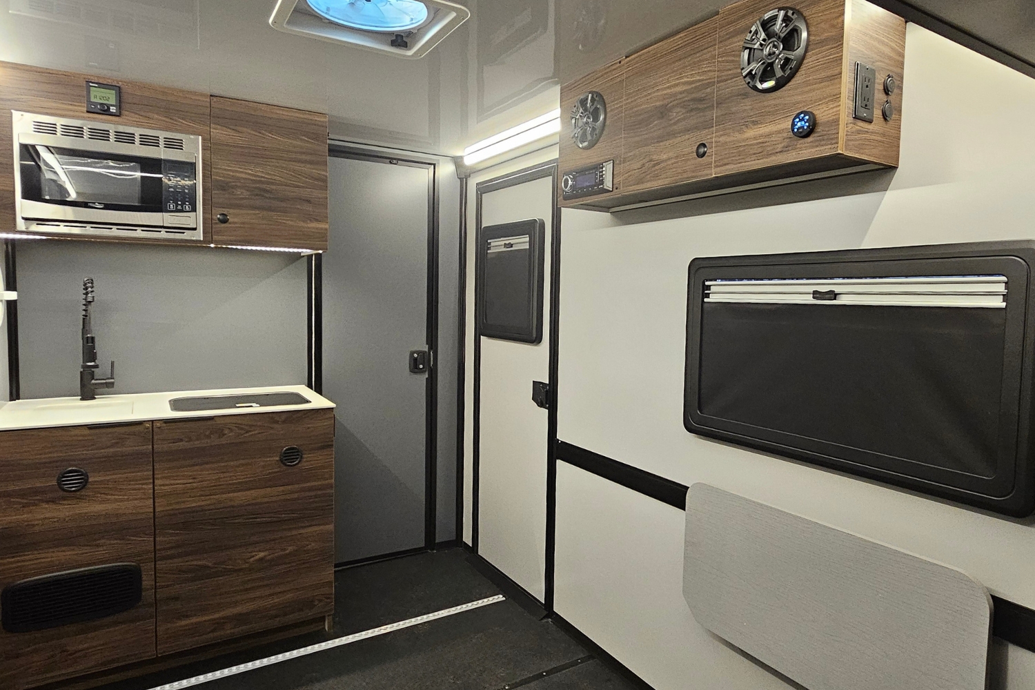 Interior view of the CORE Trailhead model. Shown standing in the rear facing forward, highlighting the entertainment cabinet, small kitchenette, front closet and side door. The wall colors are custom, white and grey for an accent.